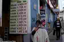 A woman walks by a sign showing the currency exchange rate in La Paz, Bolivia, Friday, June 28, 2024, two days after Army troops stormed the government palace in what President Luis Arce called a coup attempt. (AP Photo/Carlos Sanchez)