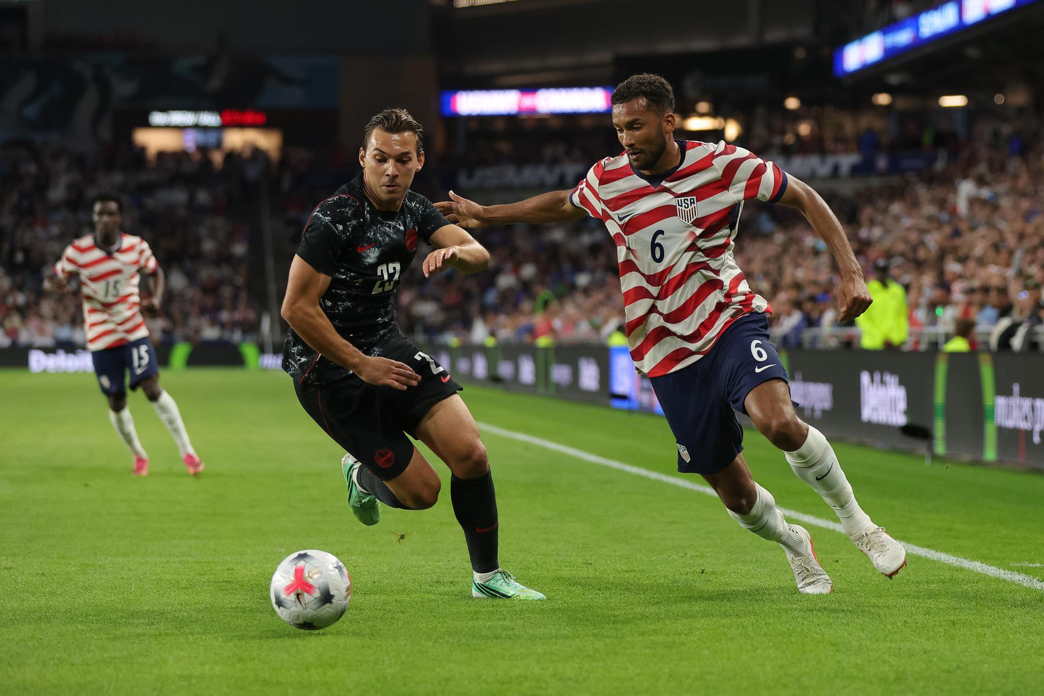 USA soccer player battles for the ball against a Canada player.