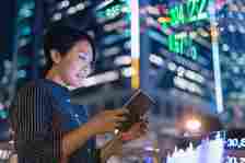 Asian businesswomen checking stock market data on tablet before Hong Kong financial display board