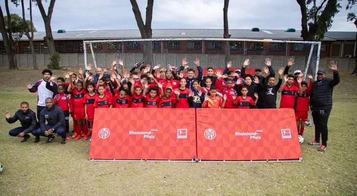 Approximately 85 youth footballers and coaches pose for a group photo behind Mainz 05 and Rheinland-Pfalz banners during the two-day international training clinic in Cape Town.