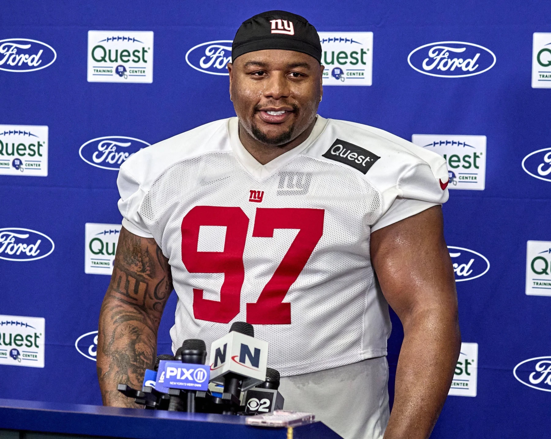 New York Giants player Dexter Lawrence (No. 97) stands at a podium with microphones during a media event, possibly discussing the team's plays ahead of the 2026 NFL Draft. Alt text generated by AI.