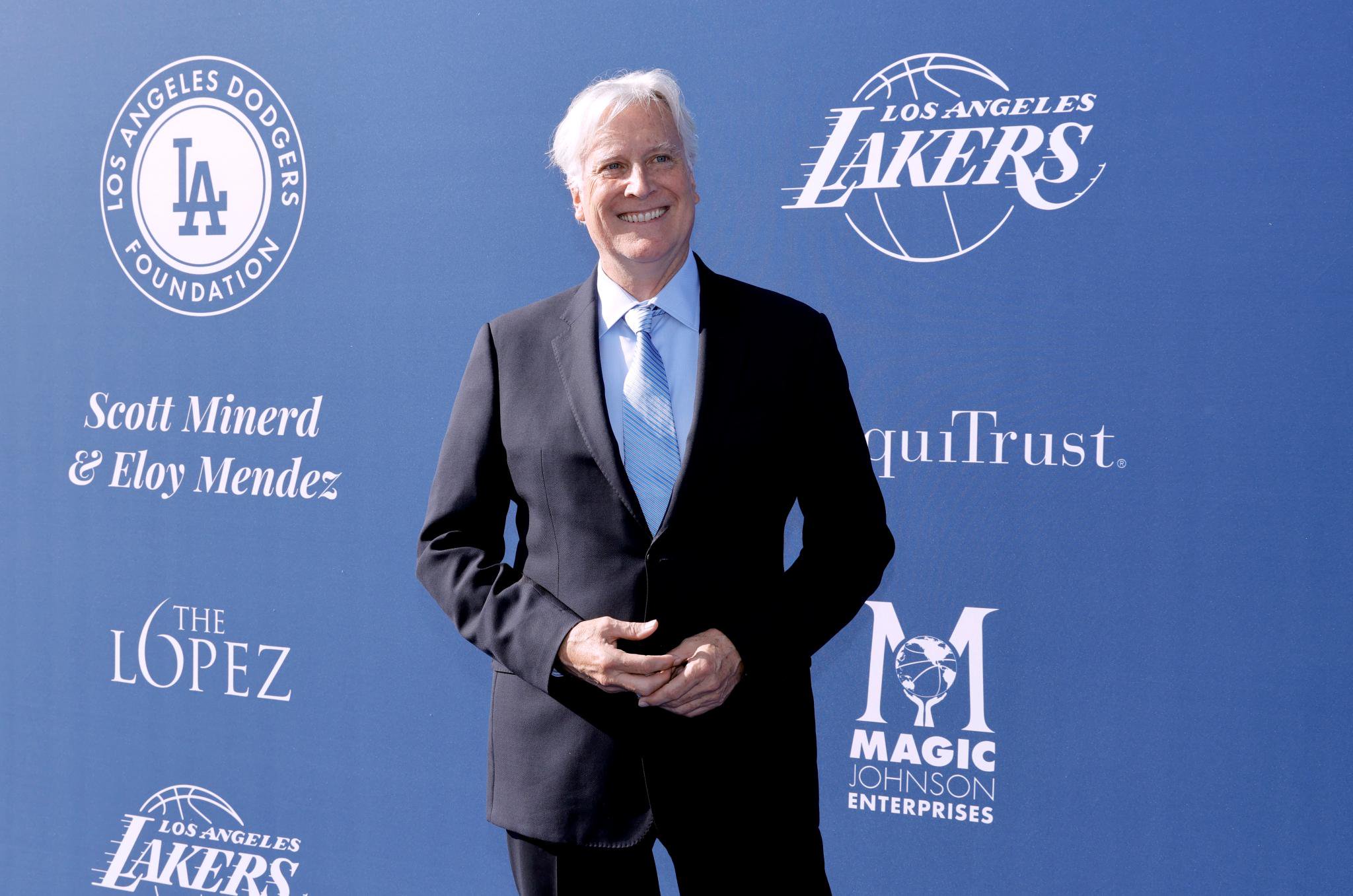 Man in a suit and striped tie standing in front of logos for the Los Angeles Dodgers Foundation, Los Angeles Lakers, and Magic Johnson Enterprises.