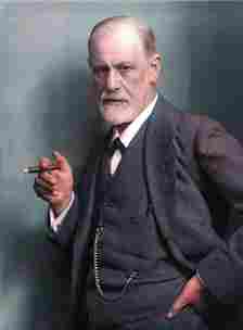 Sigmund Freud, from the waist up, wearing a dark suit and tie and holding a cigar