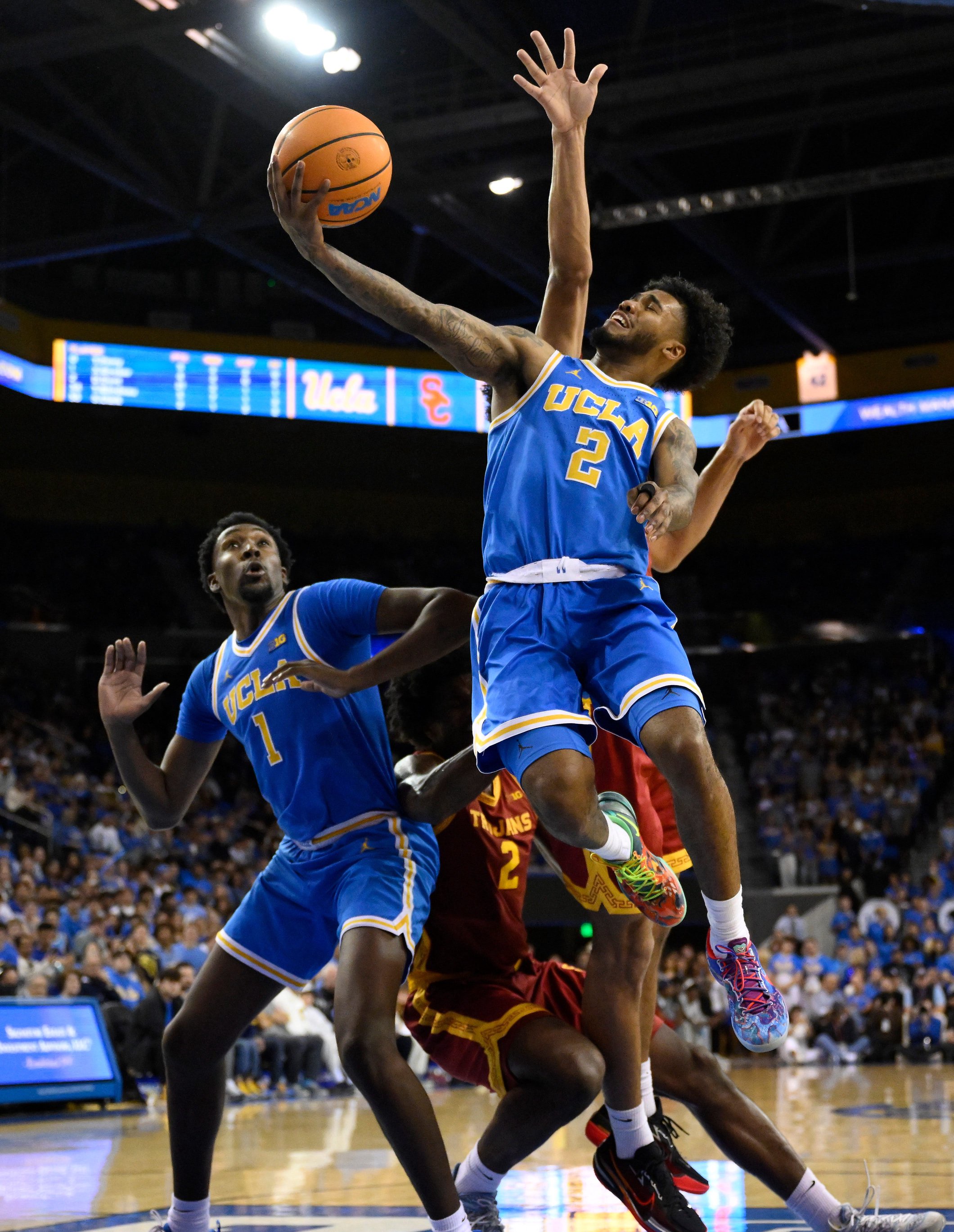 Feb 24, 2026; Los Angeles, California, USA; UCLA Bruins guard Donovan Dent (2) scores past Southern California Trojans forwards Jacob Cofie (6) and Ezra Ausar (2) during the second half tat Pauley Pavilion presented by Wescom Financial. Mandatory Credit: Robert Hanashiro-Imagn Images
