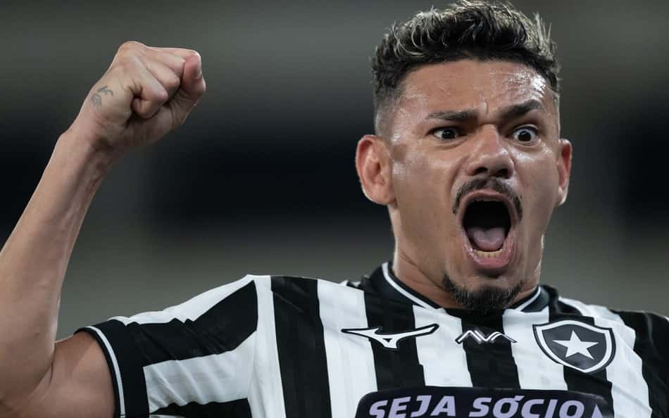 Jogador com camisa listrada preto e branco ergue o punho em celebração, boca aberta.