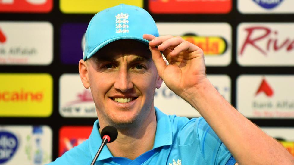 Harry Brook, wearing a blue cap, looks straight ahead while half-smiling in front of a microphone