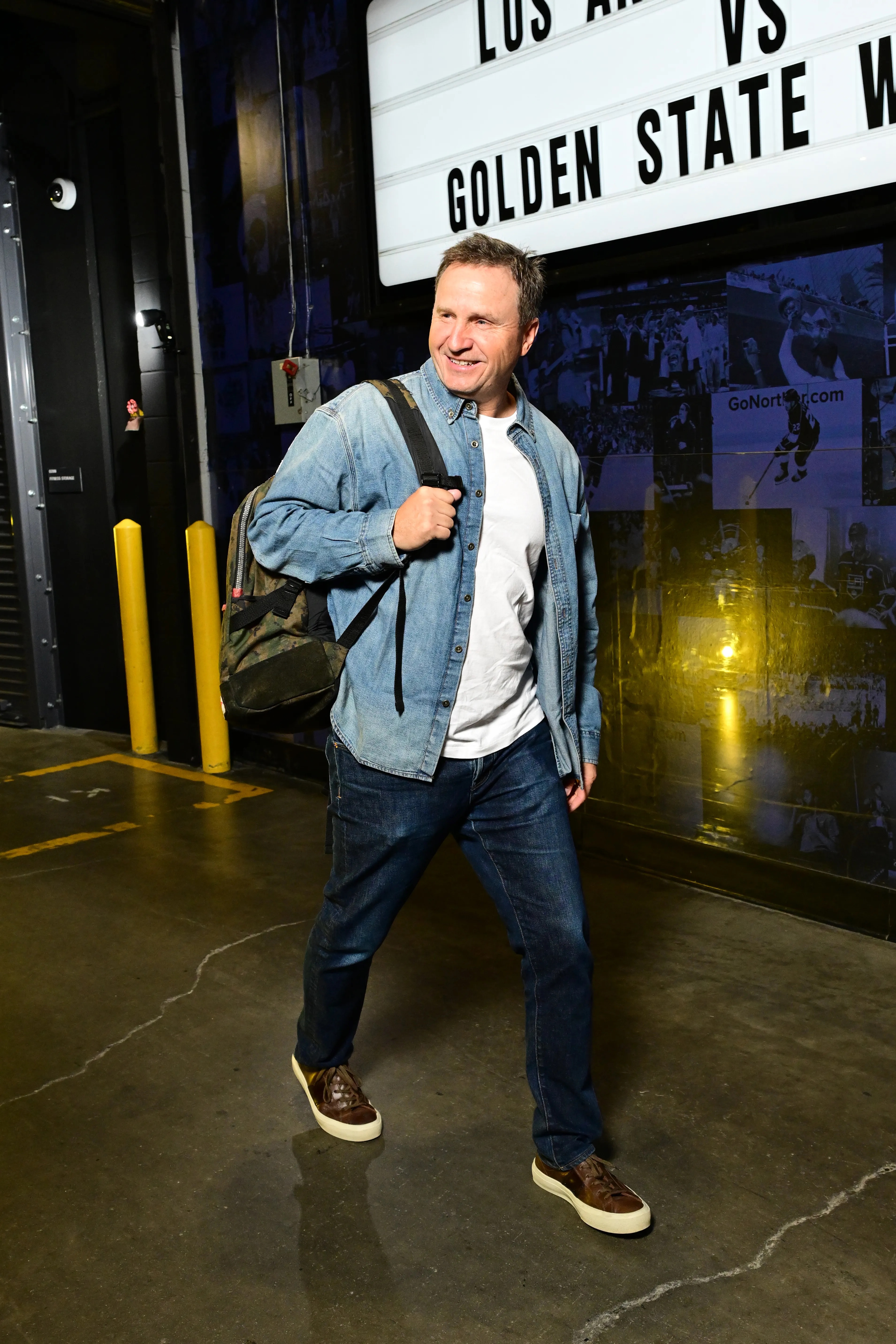 Assistant Coach Scott Brooks arrives at the arena wearing a denim shirt, white t-shirt, jeans, and a backpack.