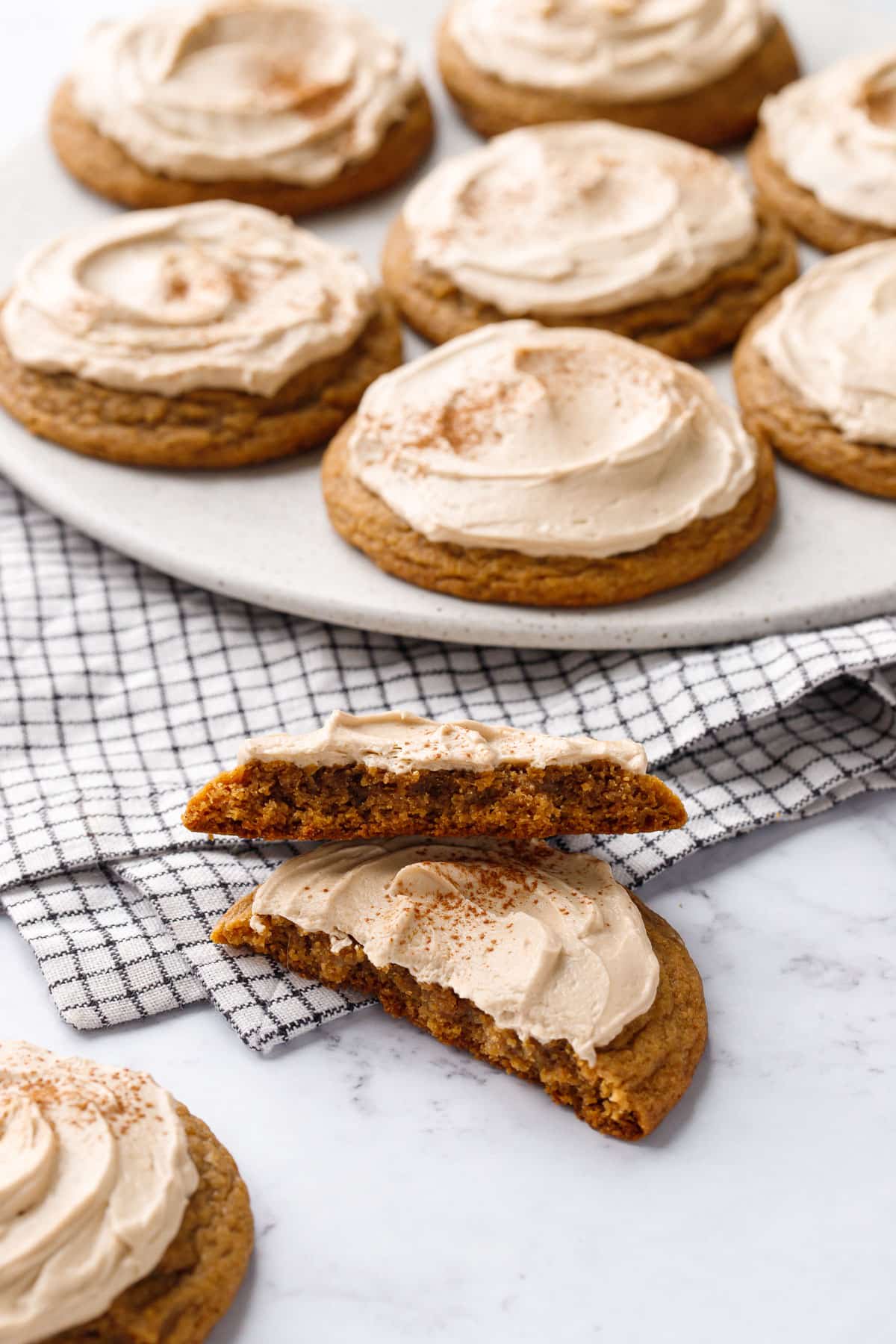 Plate of Caramel Pumpkin Cookies with Salted Caramel Frosting, one cookie in the foreground broken in half to show the chewy texture inside.