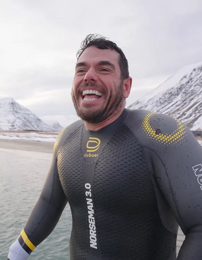 Extreme swimmer smiling in a wetsuit in front of snowy mountains.