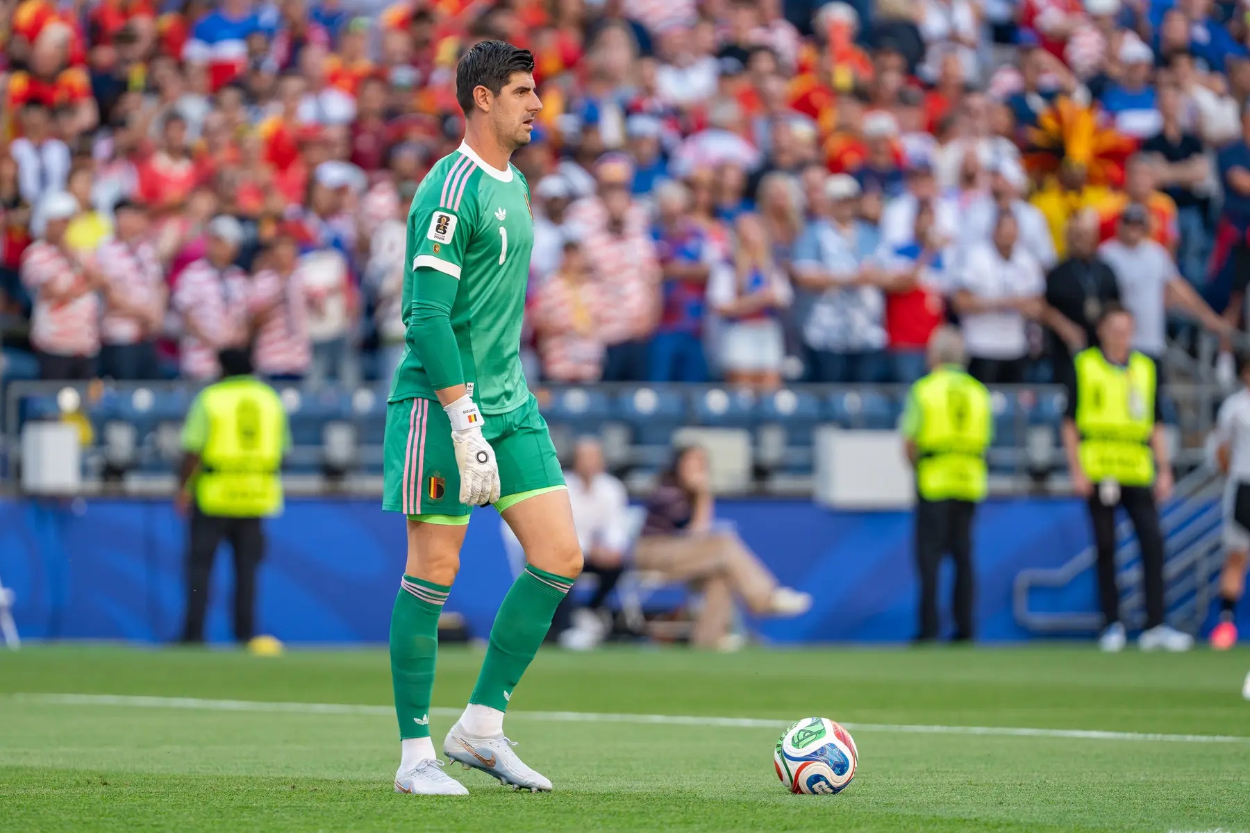 Thibaut Courtois in a green Belgium national team goalkeeper kit on a football pitch.