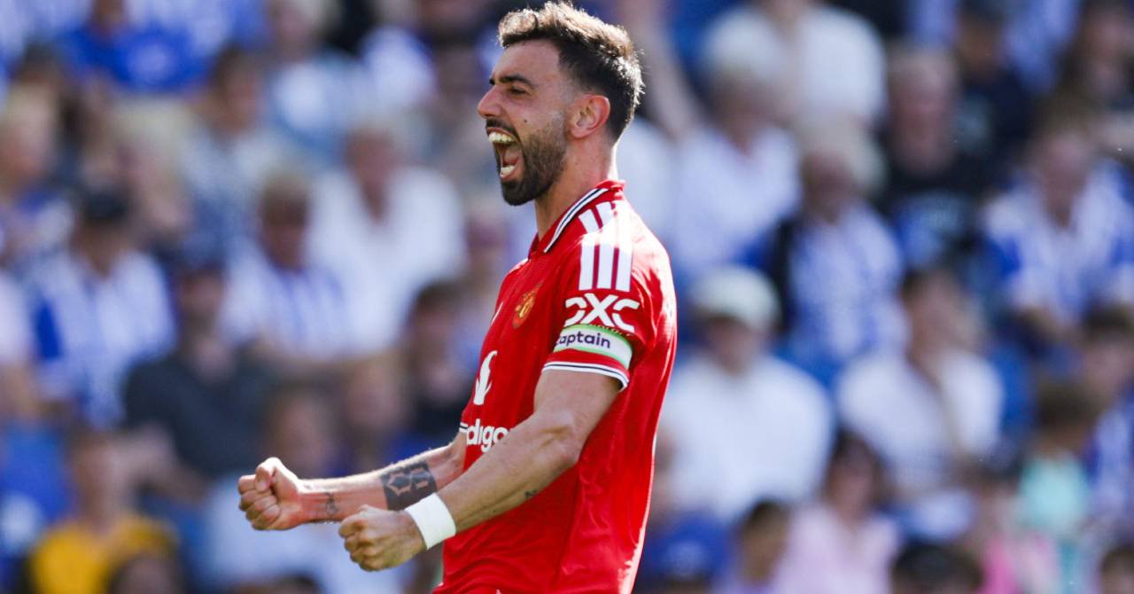 Portugal footballer Bruno Fernandes raising both arms and looking to his left while celebrating a goal for Premier League team Manchester United Football Club in a red shirt with white and black trim