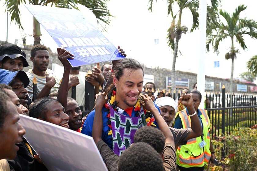 A fan presents Jarome Luai with a bilum  as a welcome gift while others hold banners.
