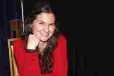 lisa jakub at a 2021 convention, wearing a red jumper and smiling at the camera