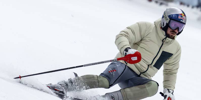 Skifahrer mit Helm und Skibrille fährt rasant eine verschneite Piste hinab.