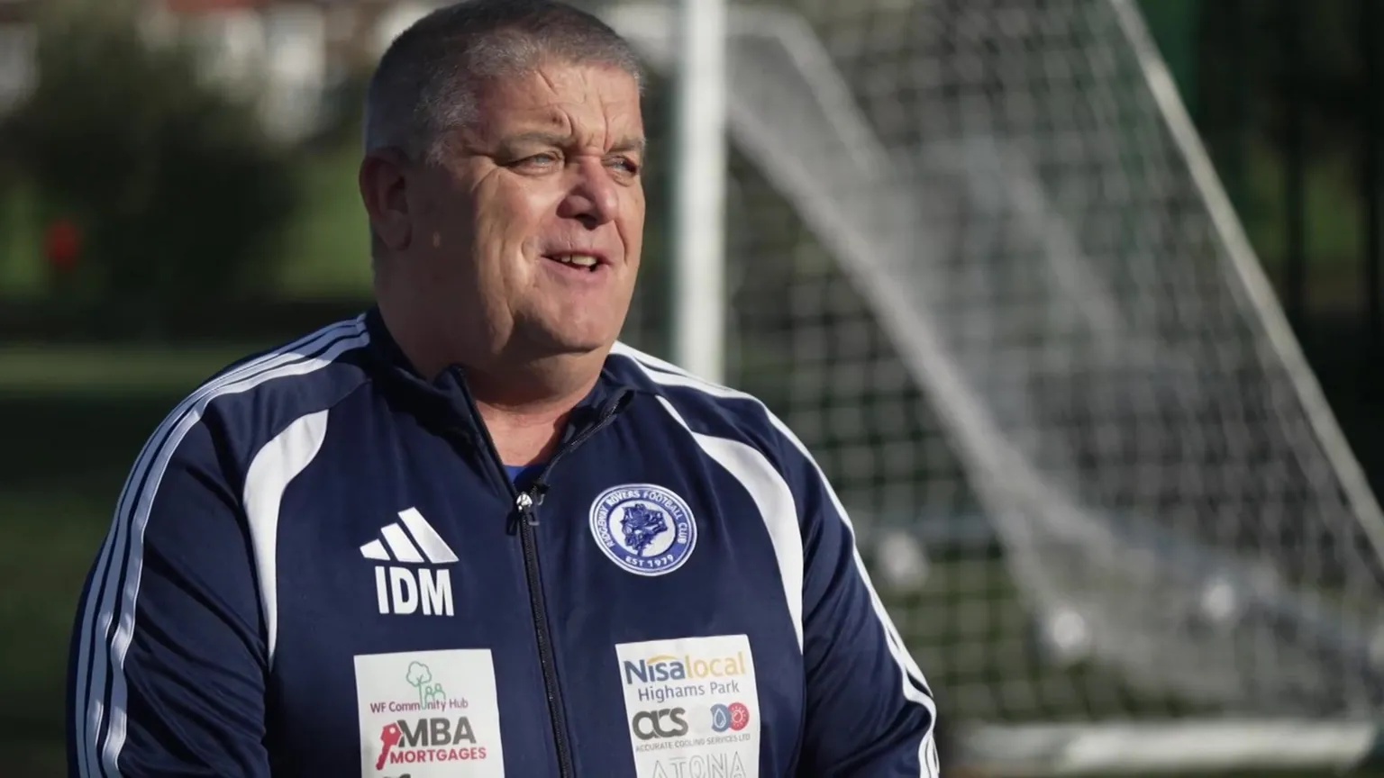 BBC Ian Marshall in a navy Ridgeway Rovers FC sports jacket standing in front of a football goal.