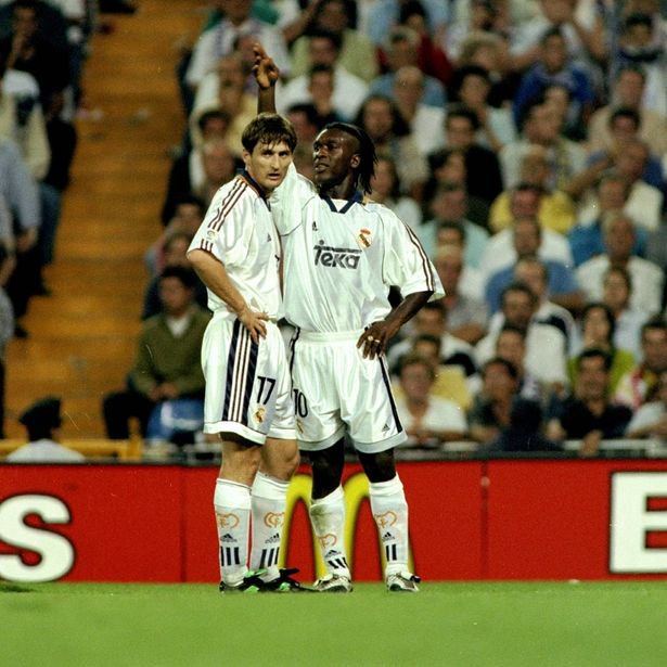 Two athletes in white uniforms celebrate a victory on the field in front of a cheering audience.