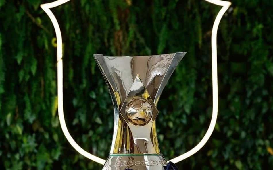 Troféu do Brasileirão com esfera dourada no centro, diante de escudo iluminado ao fundo.
