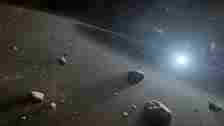 Asteroid Day: Space scene with many floating rocks illuminated with light from distant sun.