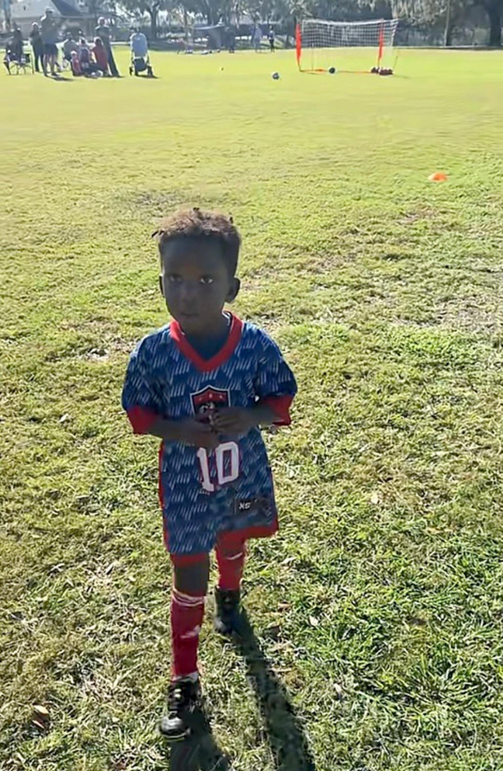 A 3-year-old boy in a soccer uniform walking on a field.