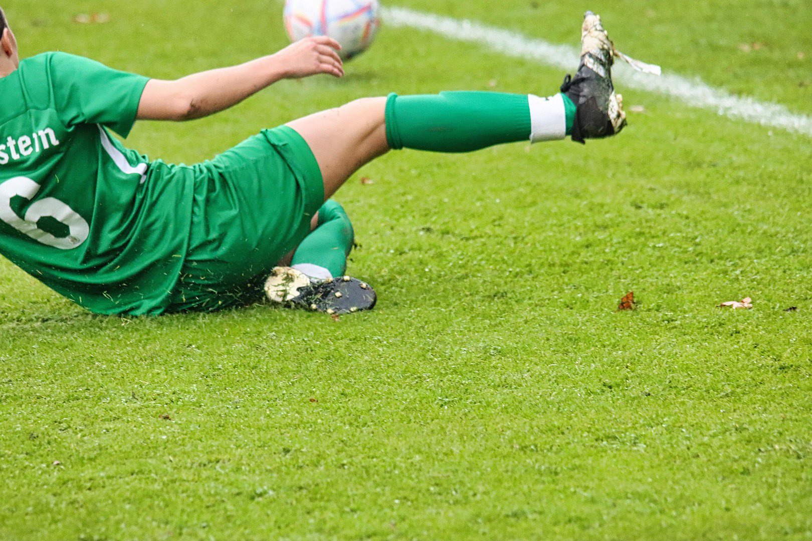 Fußballspieler in grünem Trikot mit einer Grätsche