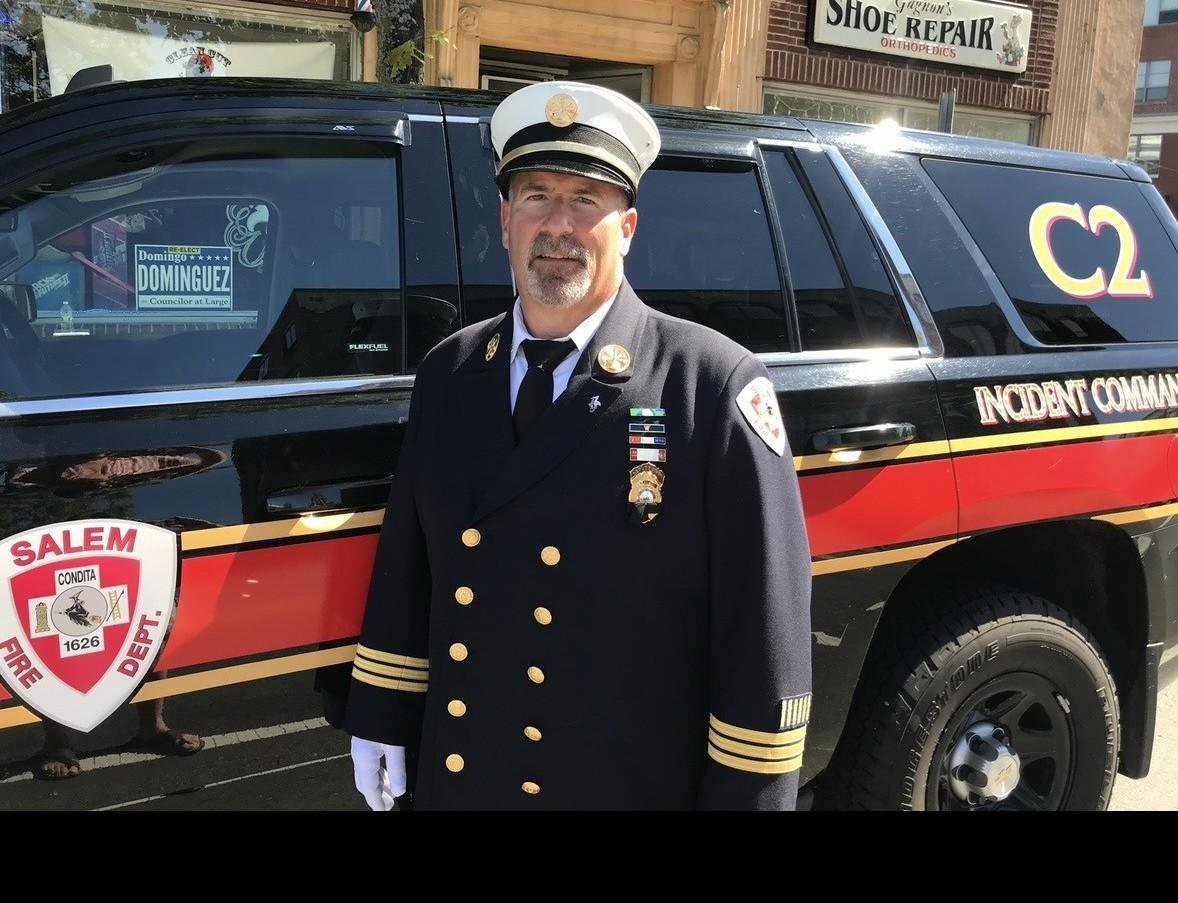 Retired Massachusetts fire chief Dennis LeVasseur stands in uniform in front of an incident command vehicle.