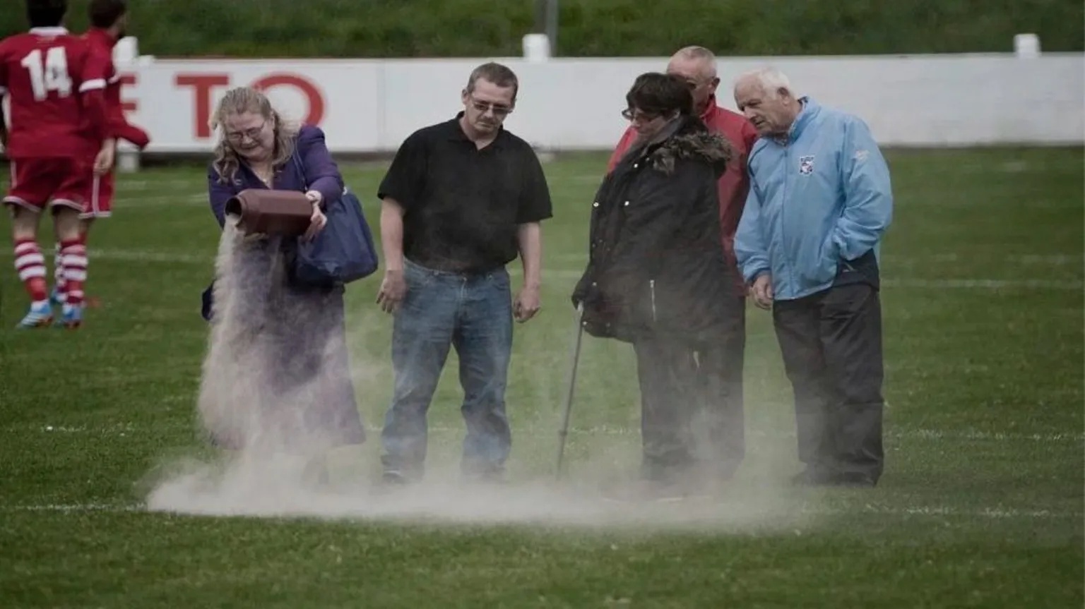 Peter Robinson People stood on a football pitch drop ashes from an urn onto the pitch. There are five people in a group and one woman looks to be upset
