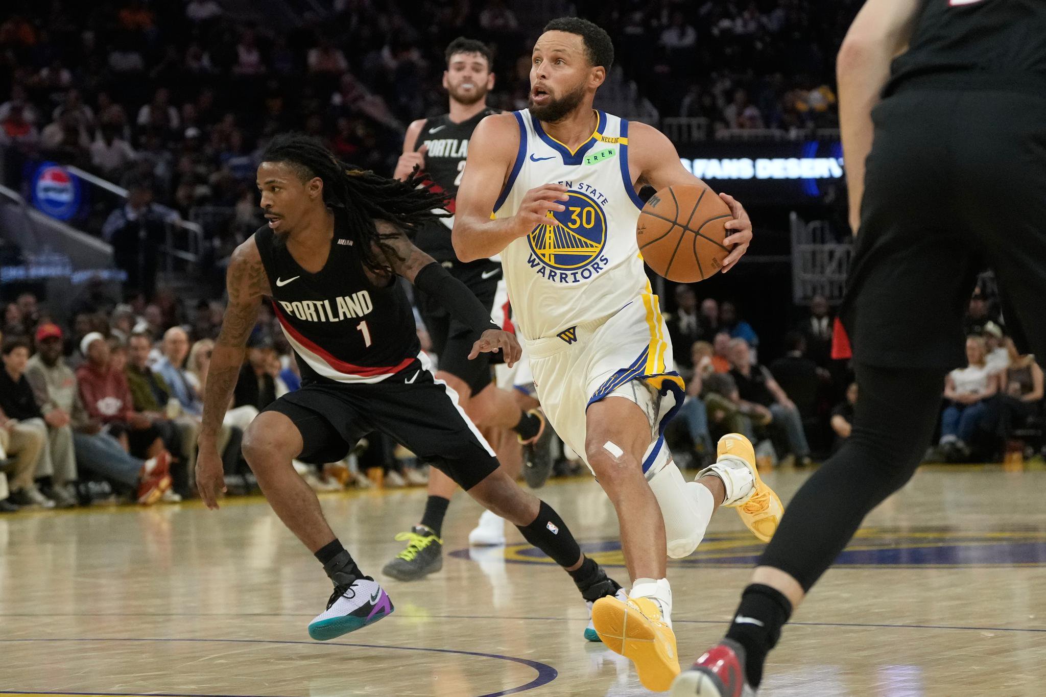 Stephen Curry dribbles the ball down the court while guarded by Ja Morant.