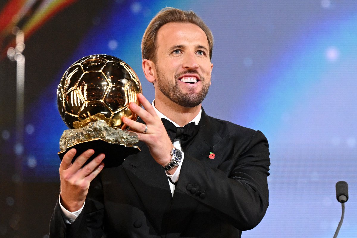 Harry Kane in a tuxedo, holding a golden football trophy, wearing a Rolex Daytona watch.