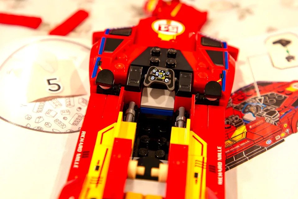 Close-up of a red LEGO vehicle cockpit with control panel and instruction sheet in the background.