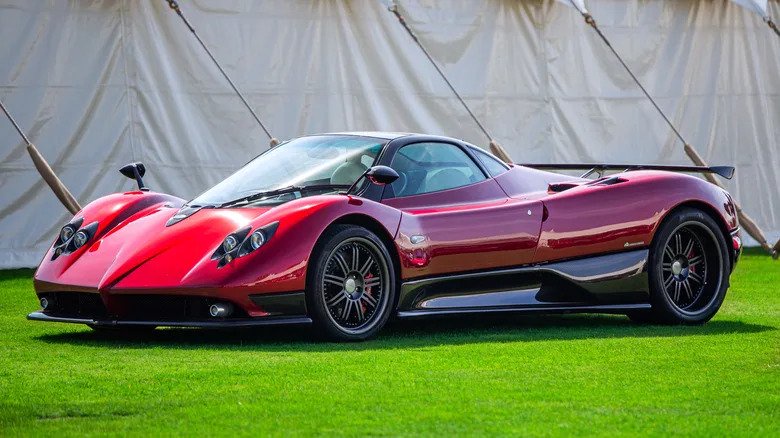 A red Pagani Zonda parked on a lawn with a large tent in the background