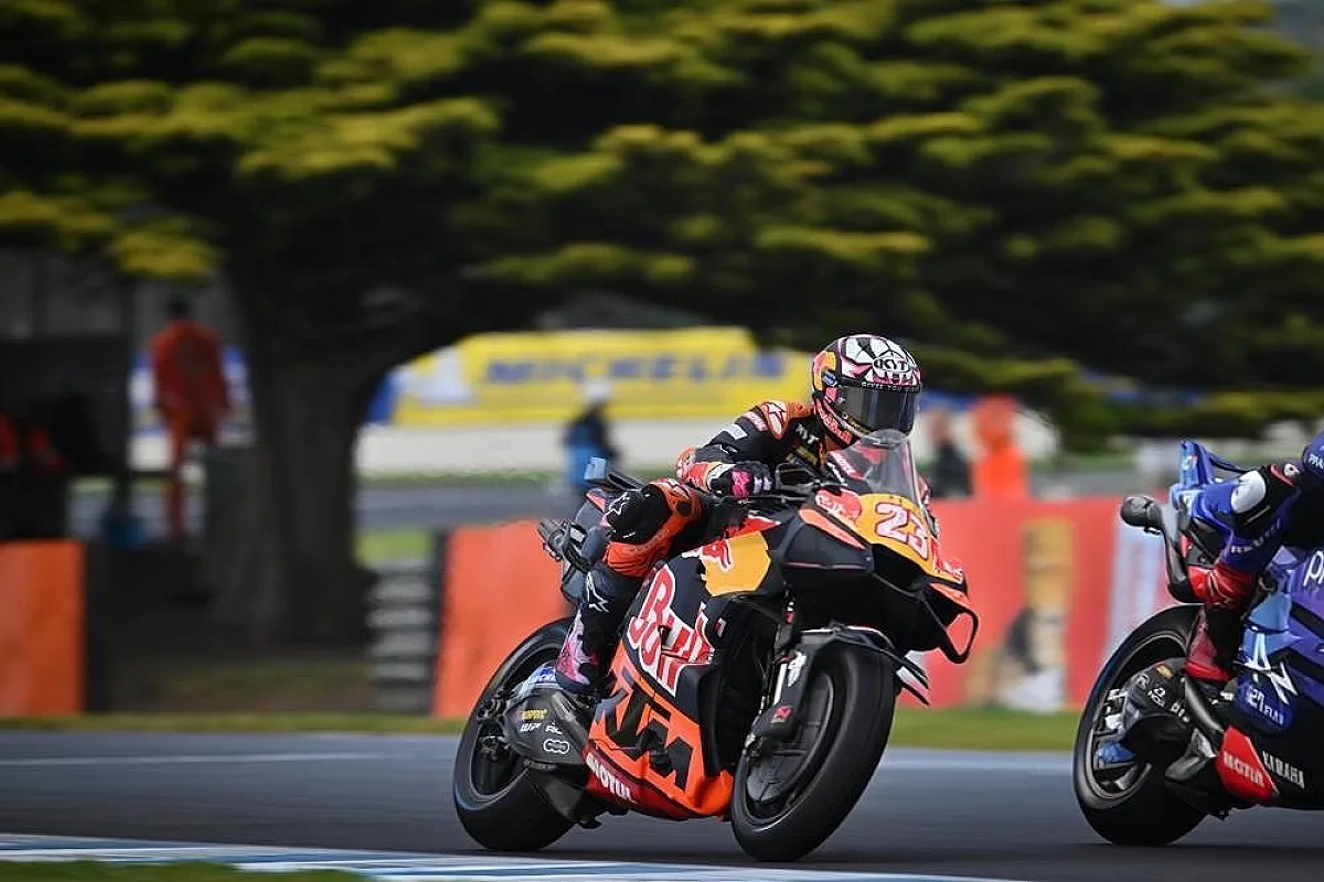 KTM MotoGP rider number 23 in Red Bull livery leaning through a corner at a track, with a rival bike in blue beside him