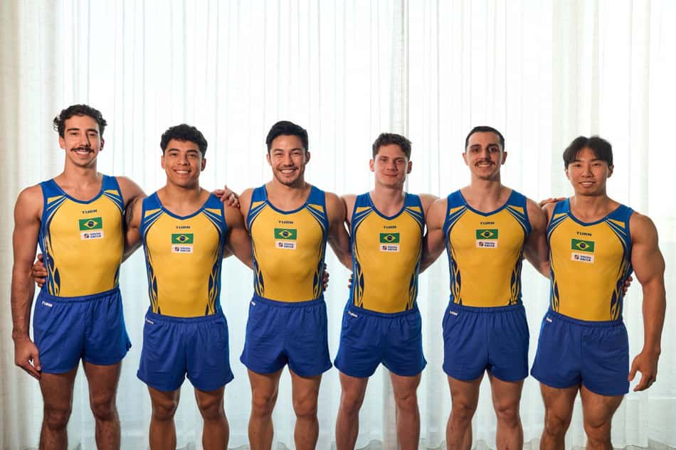 Seis ginastas da equipe de ginástica do Brasil, com uniformes amarelos e azuis, lado a lado.