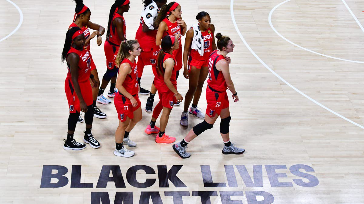 Atlanta Dream players walk by a Black Lives Matter graphic on the court.