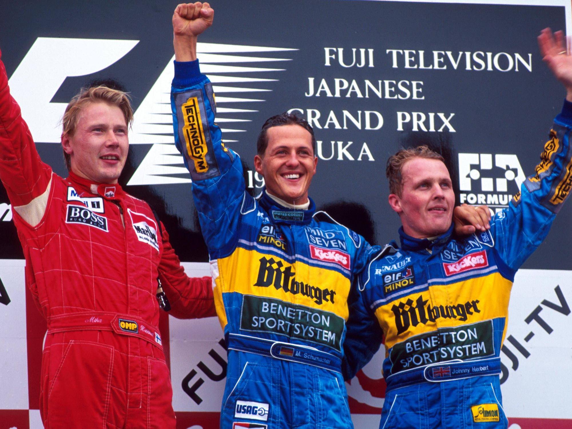 Mika Häkkinen, Michael Schumacher und Johnny Herbert stehen nebeneinander auf dem Podest und winken.