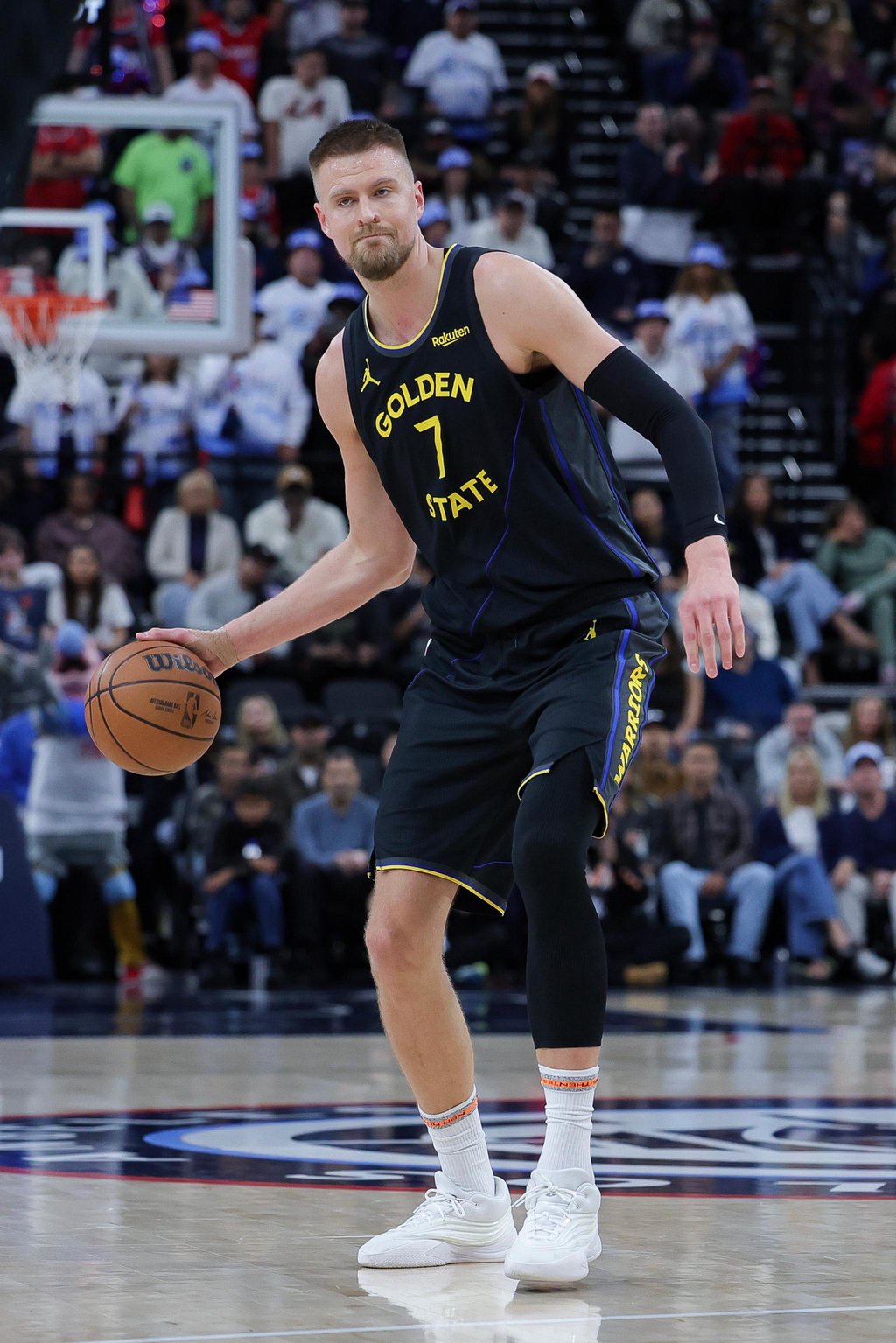 A basketball player wearing a Golden State Warriors jersey dribbles the ball during a game.