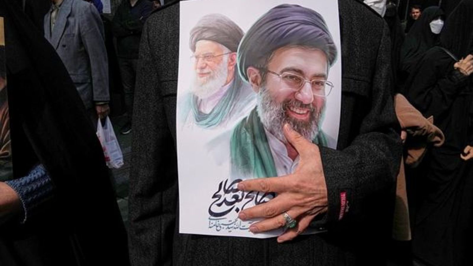 A mourner holds a poster depicting Ayatollah Mojtaba Khamenei, right, the successor to his late father Ayatollah Ali Khamenei, left, as supreme leader, during the funeral procession for senior Iranian military officials and civilians killed during the U.S.-Israel campaign