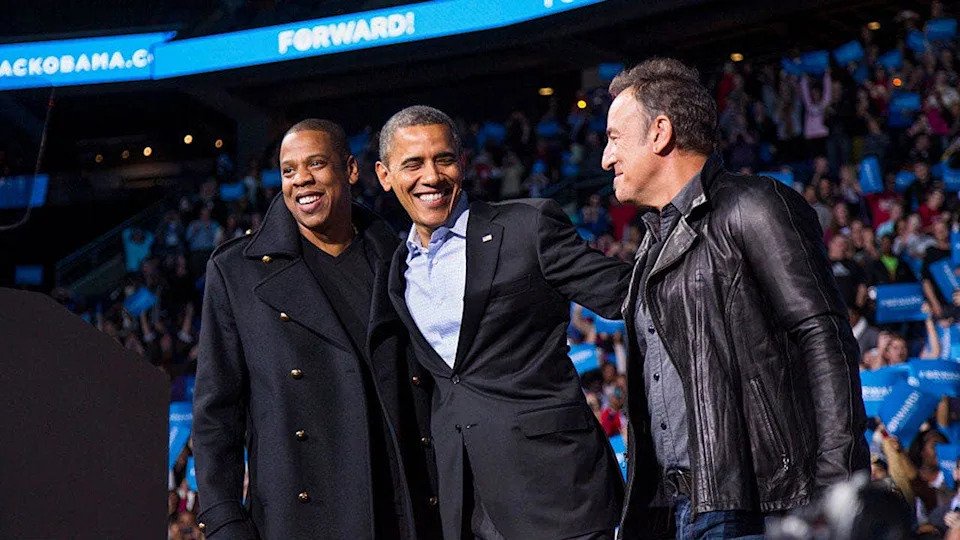 Barack Obama stands on stage with Jay-Z and Bruce Springsteen at a campaign rally.