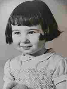 Black-and-white portrait of a young girl with short dark hair and a fringe, wearing a collared dress, holding a soft toy.