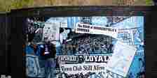 Huddersfield Town fan stands against a club mural.