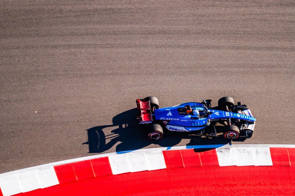 Alex Albon's blue Williams F1 car with red rear wing cornering on a red-and-white kerb at the Austin circuit