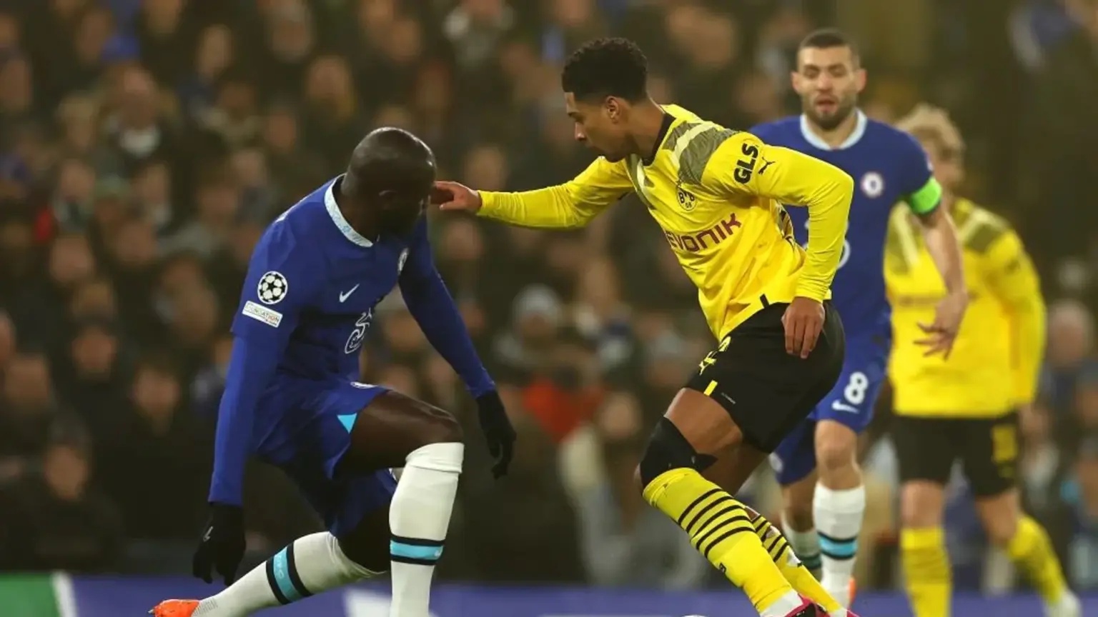 Jude Bellingham in a yellow Borussia Dortmund kit playing against a Chelsea player in a blue kit.