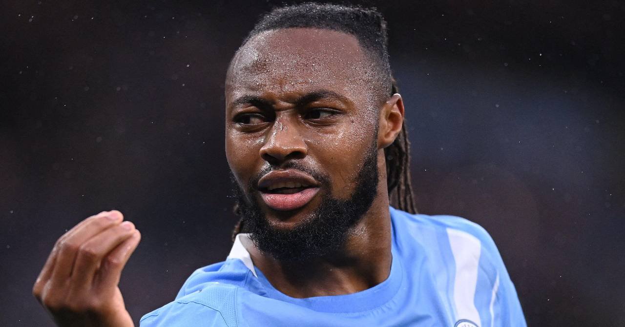 Ghana footballer Antoine Semenyo raising his right hand to celebrate a goal while playing for Premier League team Manchester City Football Club in a stadium in a light blue and white kit