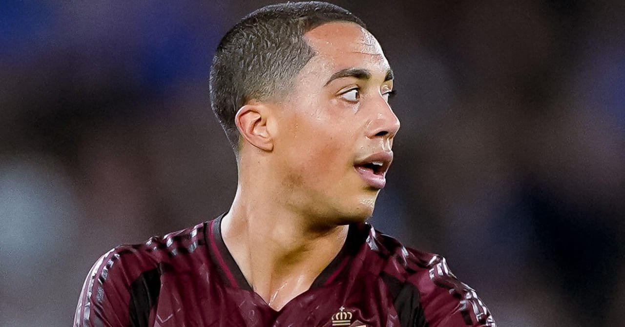 A photo of footballer Youri Tielemans looking to his left while standing on a pitch smiling and playing for the Belgium national football team in a maroon shirt