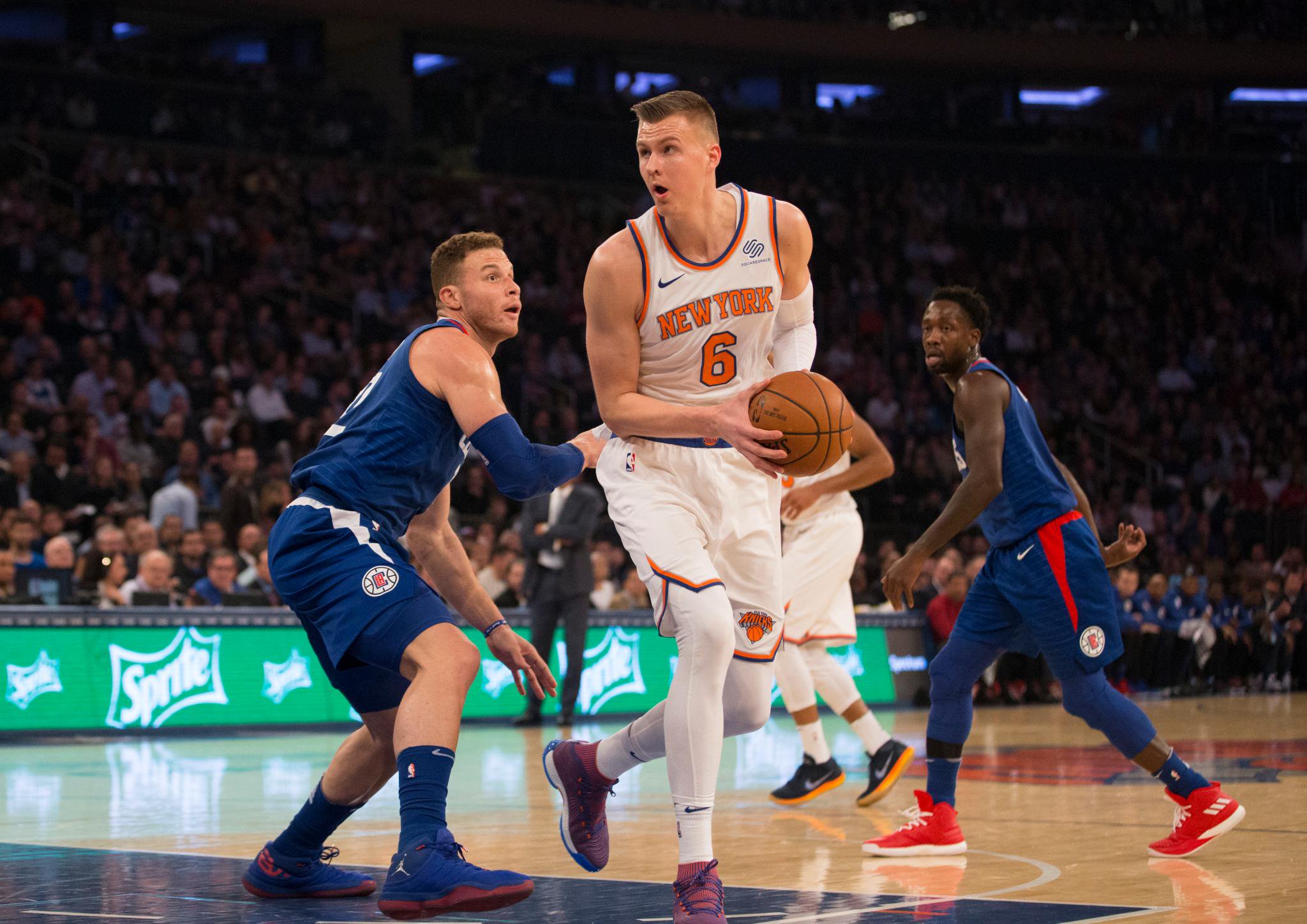 Kristaps Porzingis of the New York Knicks dribbles the ball past LA Clippers defenders during a game.
