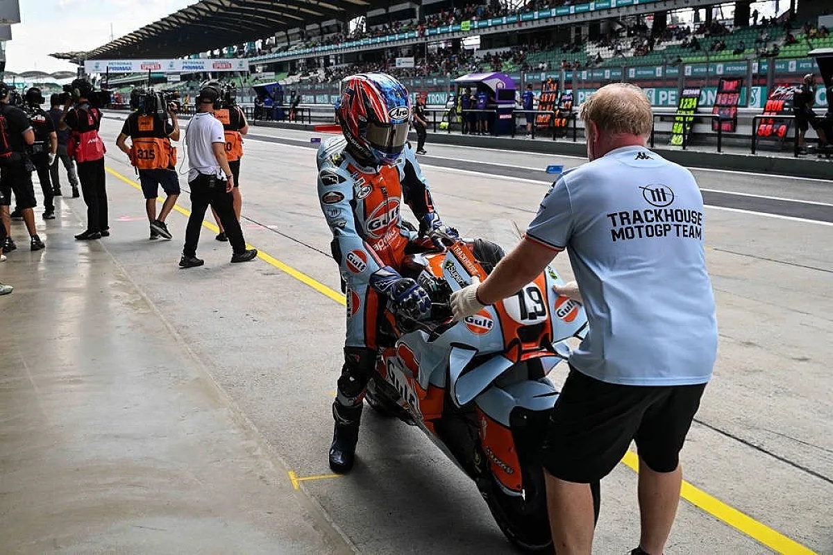 Ai Ogura in Trackhouse MotoGP colours, pushing his bike through the Sepang pit lane, with a team crew member helping.