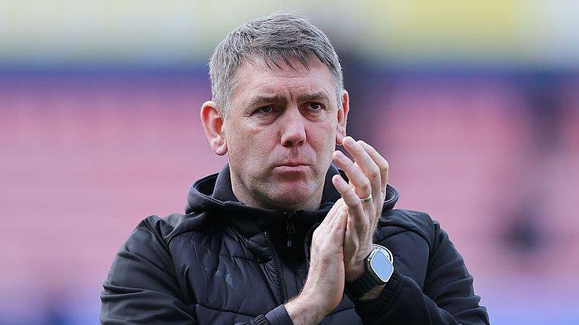 Dave Challinor applauds fans with a serious expression on his face