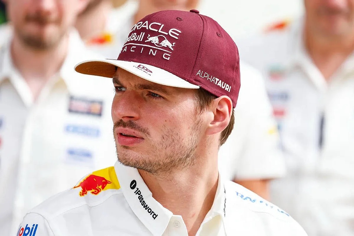 Driver in a white Red Bull Racing shirt and maroon Oracle Red Bull Racing cap with AlphaTauri branding, standing in a team paddock setting.