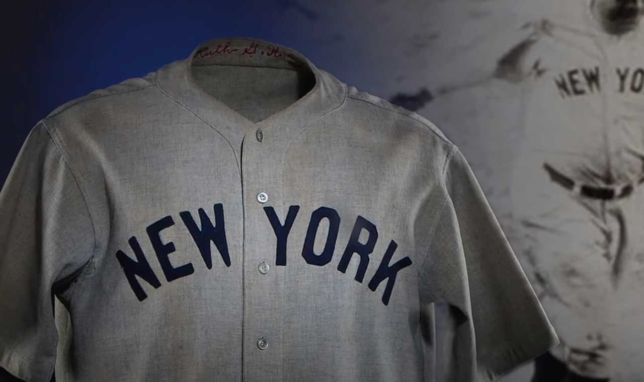 A vintage gray New York baseball jersey displayed prominently. In the background, a blurred black-and-white image shows a player in motion, also wearing a similar New York jersey.