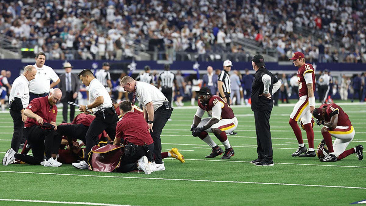 Jayden Daniels #5 lies on the field as medical staff attend to him during a game.