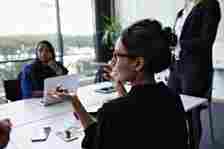 Businesswoman gesturing while discussing with colleagues during meeting at conference table in board room